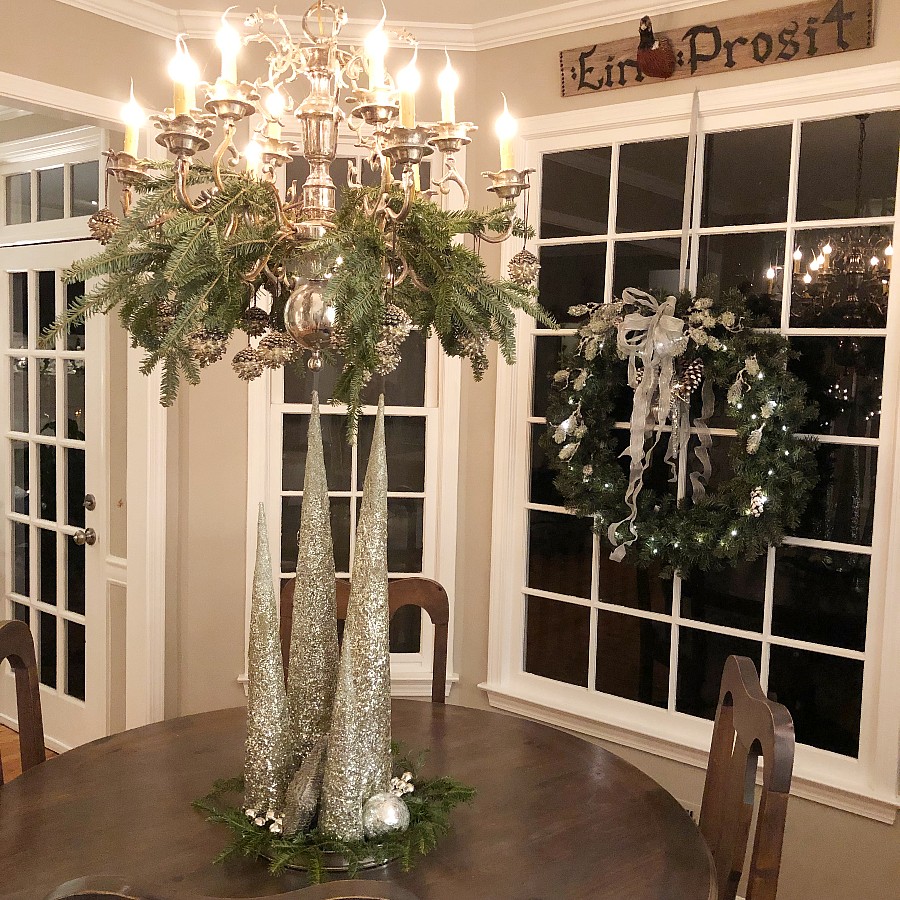 Silver chandelier with fresh greens, silver pinecones, and icicles. Silver cone trees and a large wreath.